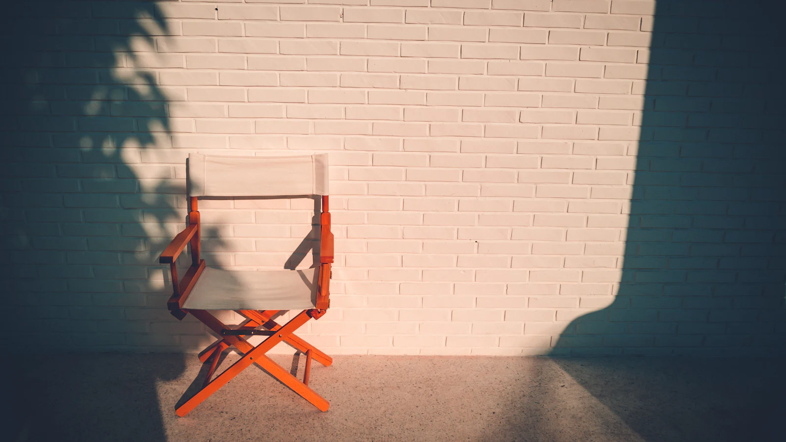 Empty director’s chair against a sunlit white brick wall, illustrating a nepo baby explainer about family connections in Hollywood